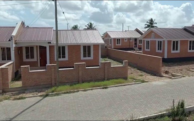Street-level view of completed NHC housing units with paved road and boundary walls