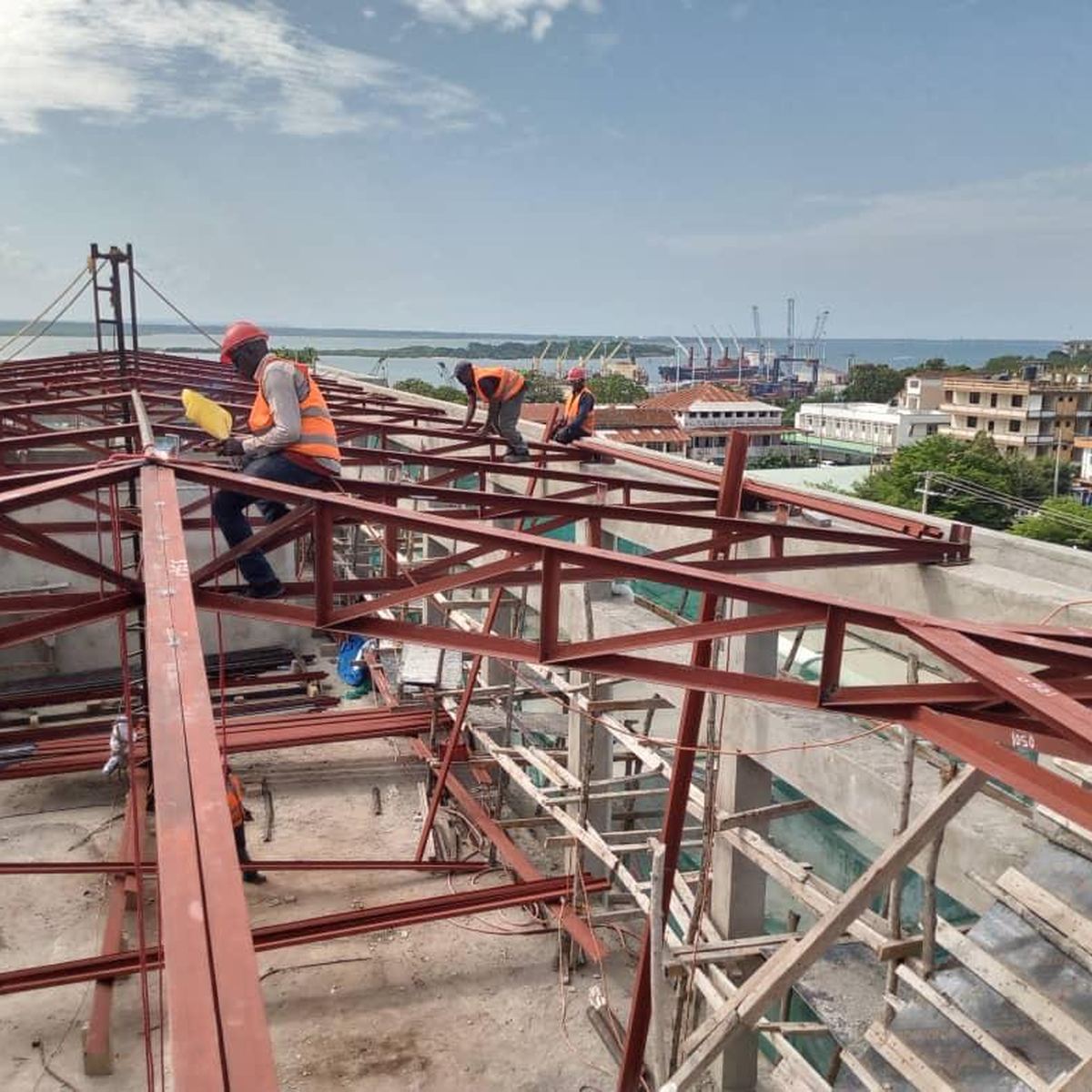 Workers positioning steel roof trusses above the building